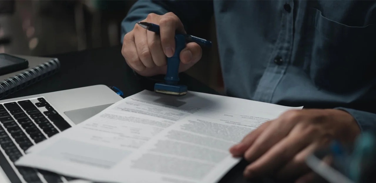 Close-up of investor stamping legal documents at Reach Group office